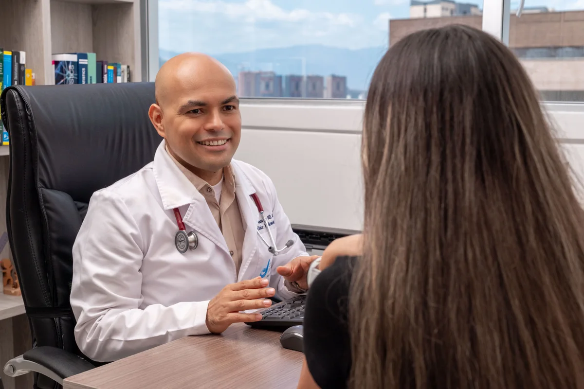Dr. Daniel Amaya sonriendo durante una consulta con una paciente en su consultorio de alergología