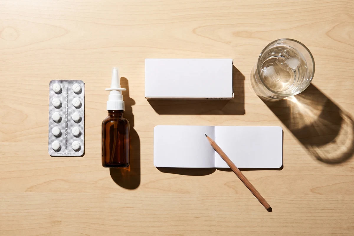 Composición de pastillas, spray nasal y vaso de agua sobre una mesa, representando la automedicación en alergias